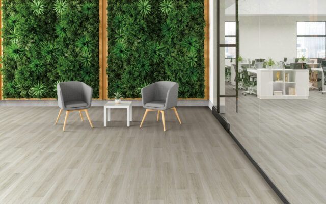 Modern lounge with two gray chairs, small white table, and green wall panels beside an open office area