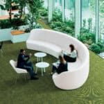 People seated on a white curved outdoor bench in a green garden lounge.