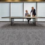 Two people stand beside a long table in a modern office or conference room.
