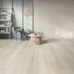 Bright empty room with light wood floor, sheer curtains, and a shelf, chair, and basket near the wall