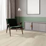 A dark green armchair beside a floor lamp in a minimalist room with pale walls and curtains