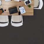 Overhead view of a wooden office desk with laptop, notebook, phone, papers, and two white chairs