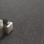 Small silver box with a dark object on top on a gray carpet.