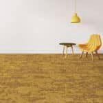 Minimal room with yellow wall, yellow chair, small table, and hanging lamp over a brown carpeted floor