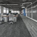 Modern office interior with desks, rolling chairs, glass walls, and patterned carpet.