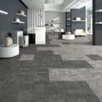 Modern office lounge with gray carpet, white seating, pendant lights, and partitioned workspaces
