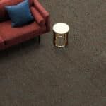 A red couch with a blue pillow beside a small round white table on dark carpet.