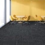 Modern meeting room with yellow wall, round table, and yellow chairs on dark carpet.