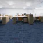 Empty office with desks and chairs on blue carpet under bright fluorescent lighting