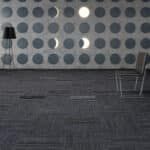 Minimalist interior with gray dotted wall, dark carpet, floor lamp, and chair by the wall