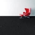 Red modern chair on a black floor against a white wall.