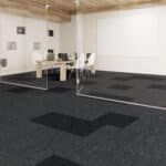 Empty modern room with dark carpet, white walls, and a small table and chairs near a window wall