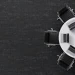 Overhead view of a white round table with black chairs on a dark floor