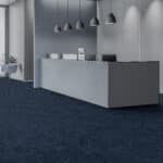 Modern minimalist lobby with a gray reception desk, pendant lights, and dark carpet.