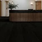Empty hotel lobby with a dark carpet and wooden front desk against beige walls.