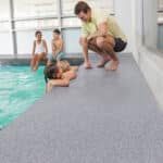 People on a pool deck helping a swimmer climb out of the water