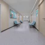 Bright hospital hallway with blue chairs, wall art, and closed doors along both sides