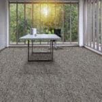 A glass-walled room with a table centered on a gray carpet, overlooking trees outside.