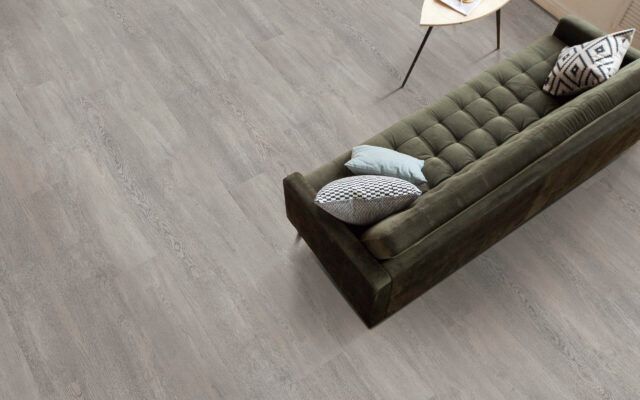 Modern living room with a green tufted sofa and decorative pillows on a gray wood floor.