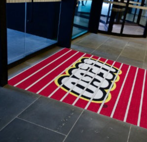 Red-and-black logo welcome mat at a glass entrance doorway