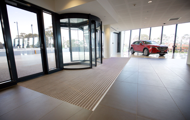 Empty lobby entrance with revolving doors, tiled floor, and a red SUV outside the glass wall
