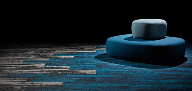 Blue cylindrical sculpture on a dark wooden floor against a black background