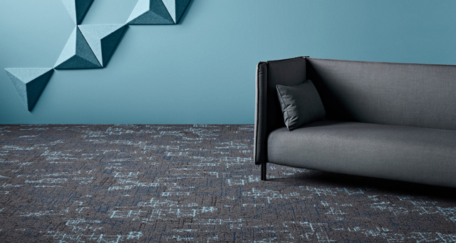 Modern living room with a gray sofa, dark patterned carpet, and teal geometric wall art