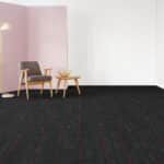 Two wooden chairs and a small table in a minimalist room with a black carpet and pale pink wall panel.