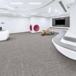 Modern white living room with gray carpet, red chairs, wall-mounted TV, and a curved staircase