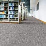 Carpeted library aisle with bookshelves and a bright hallway in the distance