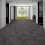 Empty indoor corridor with gray carpet leading to a bright doorway and trees outside