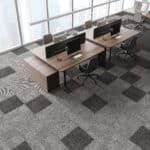 Office cubicles with wooden desks and monitors on a gray patterned carpet
