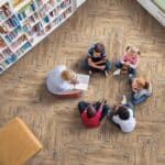 Five people sitting in a circle on a wooden floor in a library, talking and using papers.