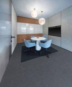 Small conference room with round white table, blue chairs, gray carpet, and white walls.