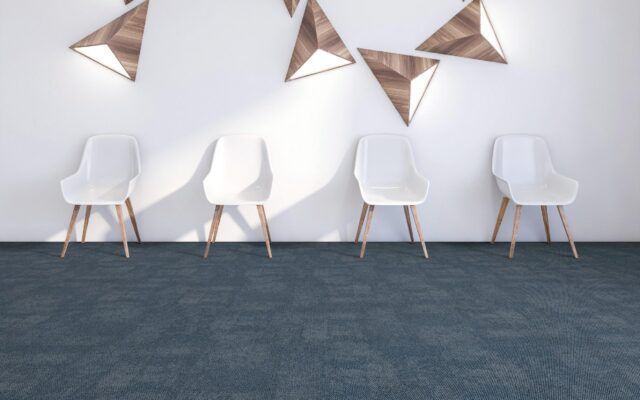 Modern waiting area with white chairs, geometric wall art, and blue carpet