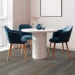 Modern dining nook with a round white table, blue chairs, and a vase on a light wood floor
