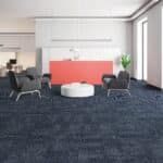 Modern office lounge with black chairs, a white ottoman, and a coral reception desk on a dark blue carpet.