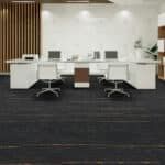 Modern office reception area with white desks, swivel chairs, and a dark carpeted floor.