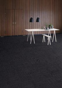 Minimal office with white desk, two black pendant lamps, and dark carpet against a wood-paneled wall.