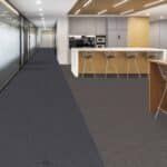 Modern office lounge with gray carpet, white walls, glass hallway, and a wood countertop kitchen area