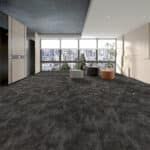 Empty modern lobby with large windows, dark carpet, white walls, and a few lounge chairs.