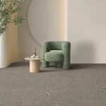 Green armchair beside a small round table in a minimalist beige room with a textured gray floor
