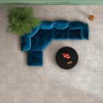 Top-down view of a teal velvet sectional, black round coffee table, and potted plant on a light rug
