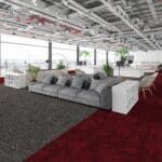Modern open office lounge with gray sofas, potted plants, and red carpet under an exposed ceiling