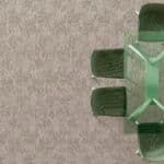 Close-up of a green plastic object with four protruding prongs on a beige carpet.