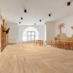 Spacious bright hall with light wood floors, white walls, arched windows, and rows of chairs along the sides