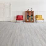 Three chairs—red, wooden cabinet, and yellow—on a light gray floor against a white wall.
