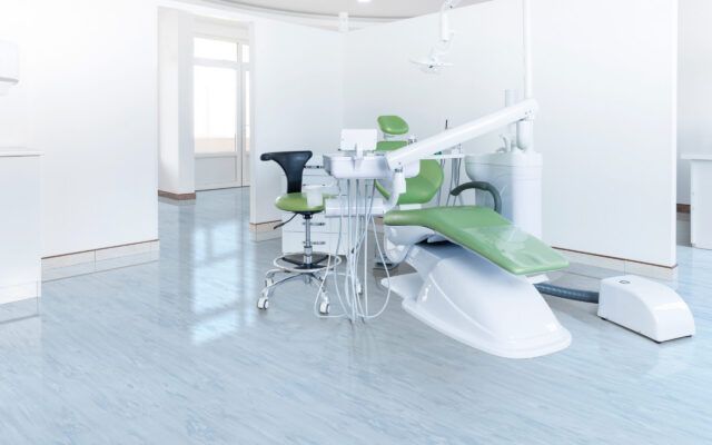 Modern dental exam room with green and white dental chair, equipment, and stools on a glossy floor