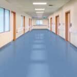 Empty office hallway with blue floor, white walls, and windows along the left side