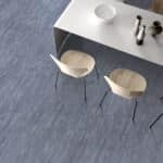 Two white chairs beside a sleek silver table on a blue carpet.